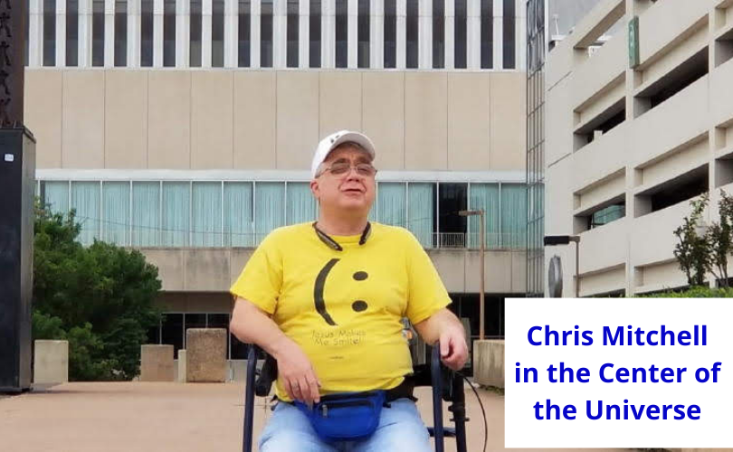 Chris Mitchell, CEO and founder of #DefineYourself, wearing a yellow happy face shirt, white ballcap, sitting on his rollator in the center of the universe in Tulsa OK