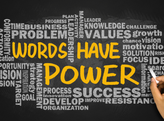 Black background with a collection of words in grey. In the center of the words, in large test and gold color appears “Words Have Power”