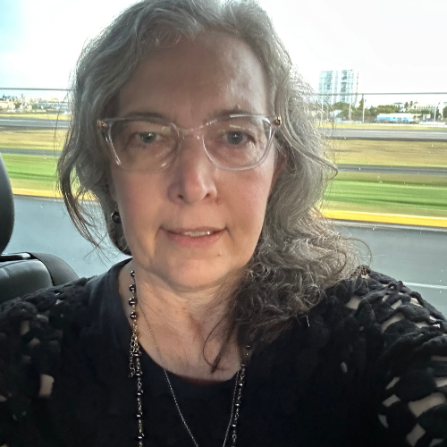 Dr. Jennifer Dal, a Caucasian woman with shoulder-length hair, glasses wearing a necklace, and a dark-colored top outside