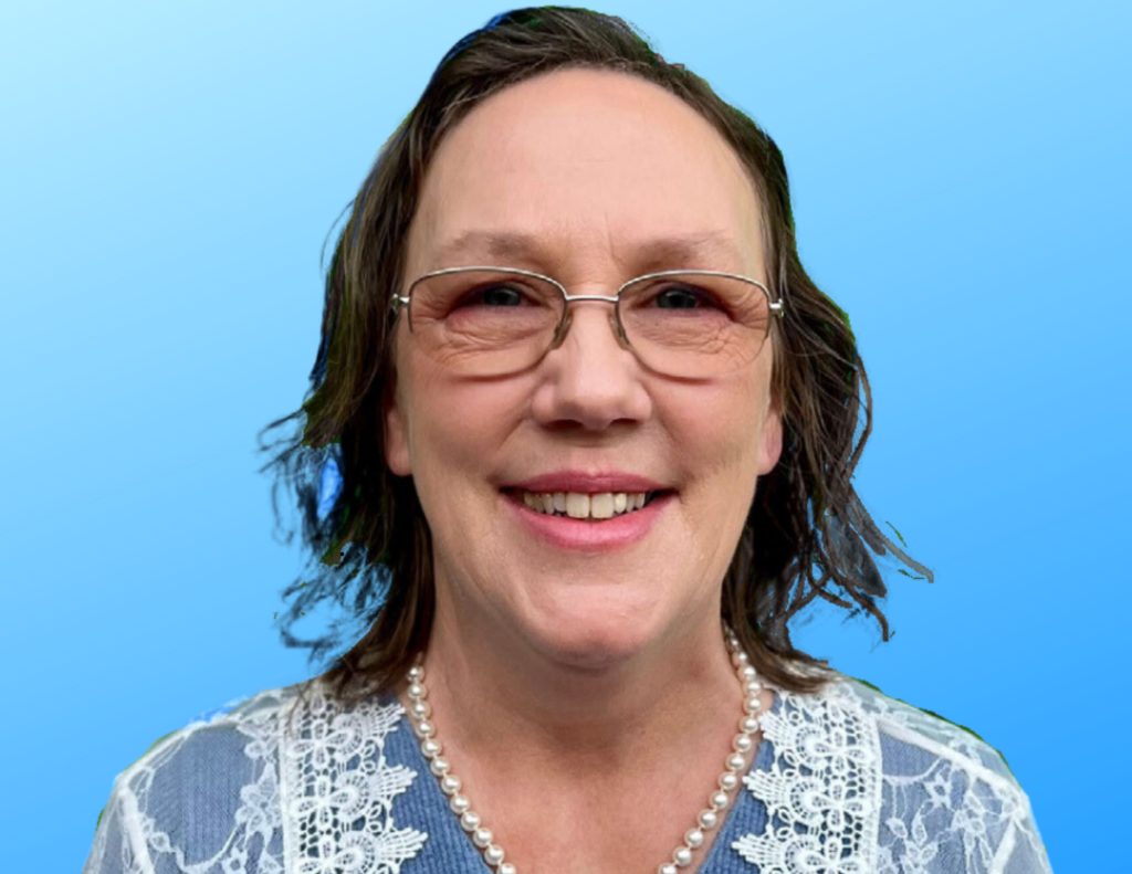 A Caucasian woman with shoulder-length hair, wearing glasses and a blue and white top smiling with a light blue background